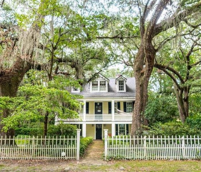 Summerville home in Augusta with light yellow exterior, a white picket fence and mossy trees